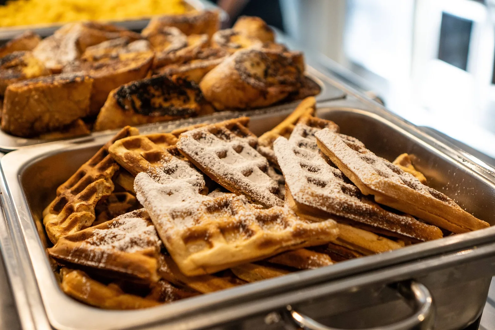A delicious breakfast buffet with golden waffles and French toast dusted with powdered sugar.